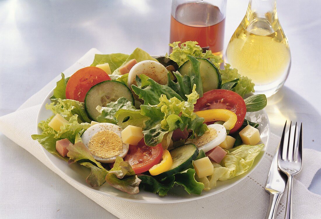 Blattsalat mit Schinken, Ei und Käse auf Teller; Essig, Öl