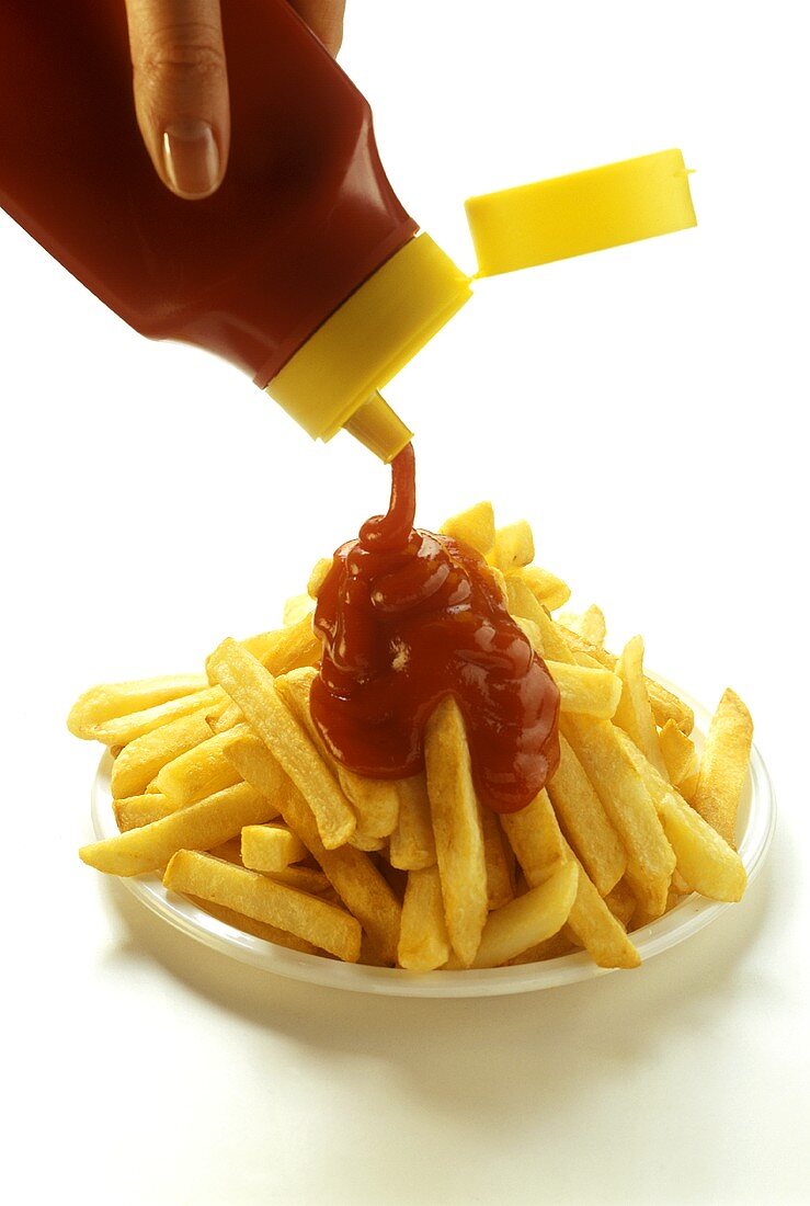 Pommes frites auf Teller mit Ketchup begiessen