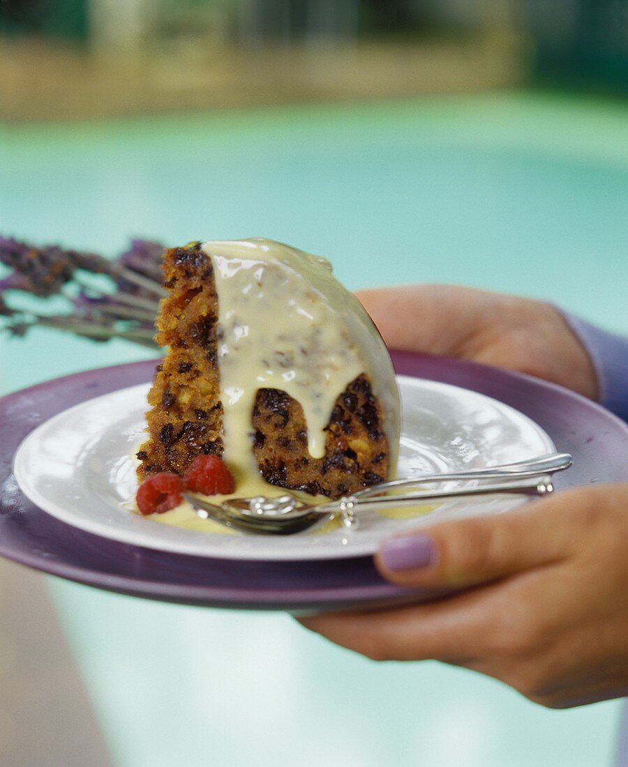 Hände halten Plumpudding mit Vanillesauce auf Teller