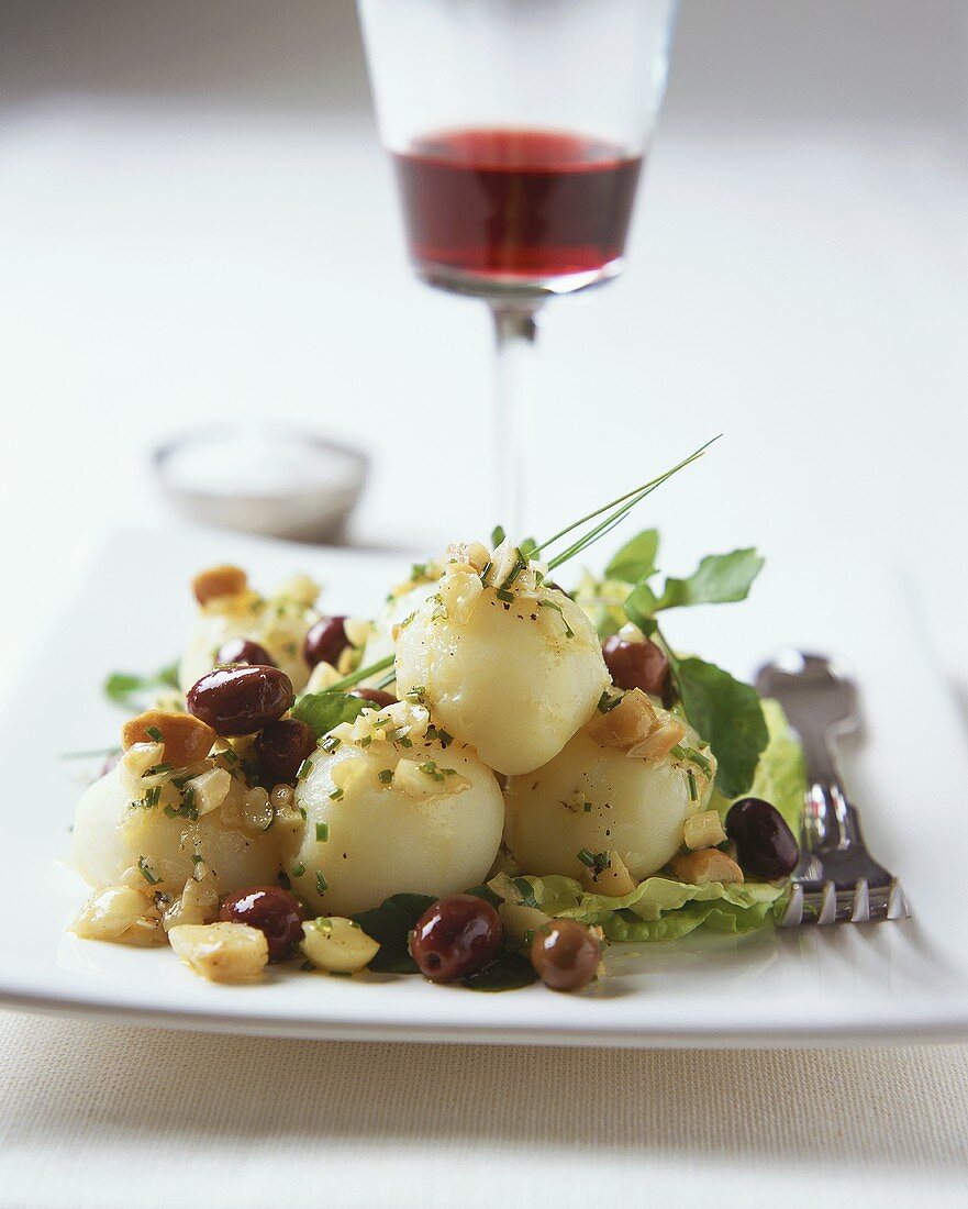 Cooked potatoes with onions and olives on salad leaves