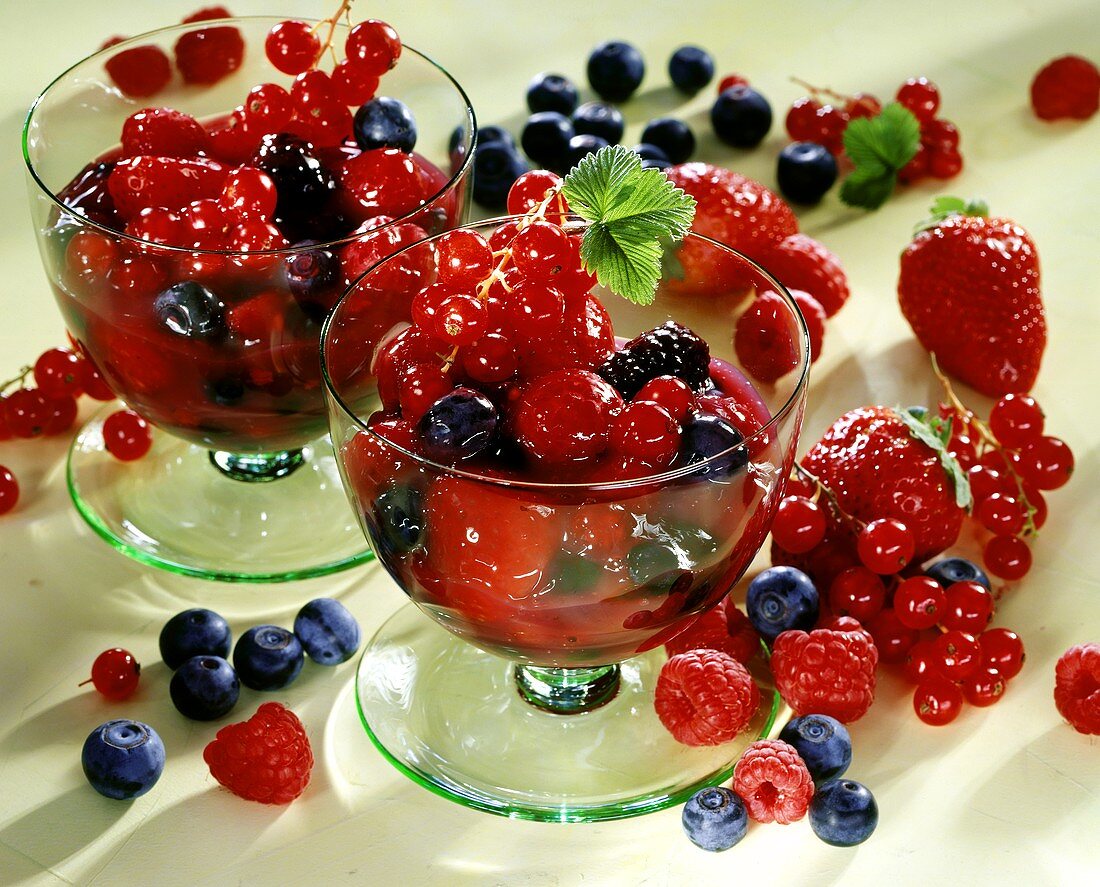 Red berry compote in two bowls, surrounded by fresh berries