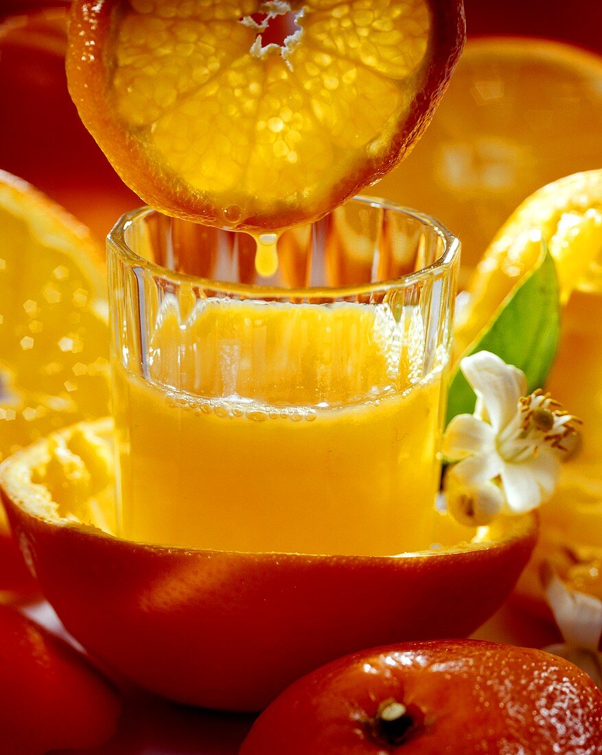 Orange juice in a glass, with orange slice above it
