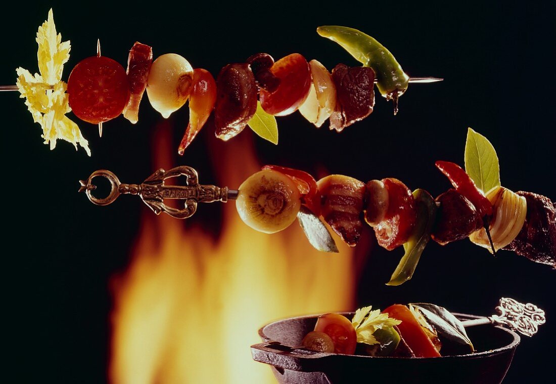 3 meat and vegetable kebabs in front of an open fire