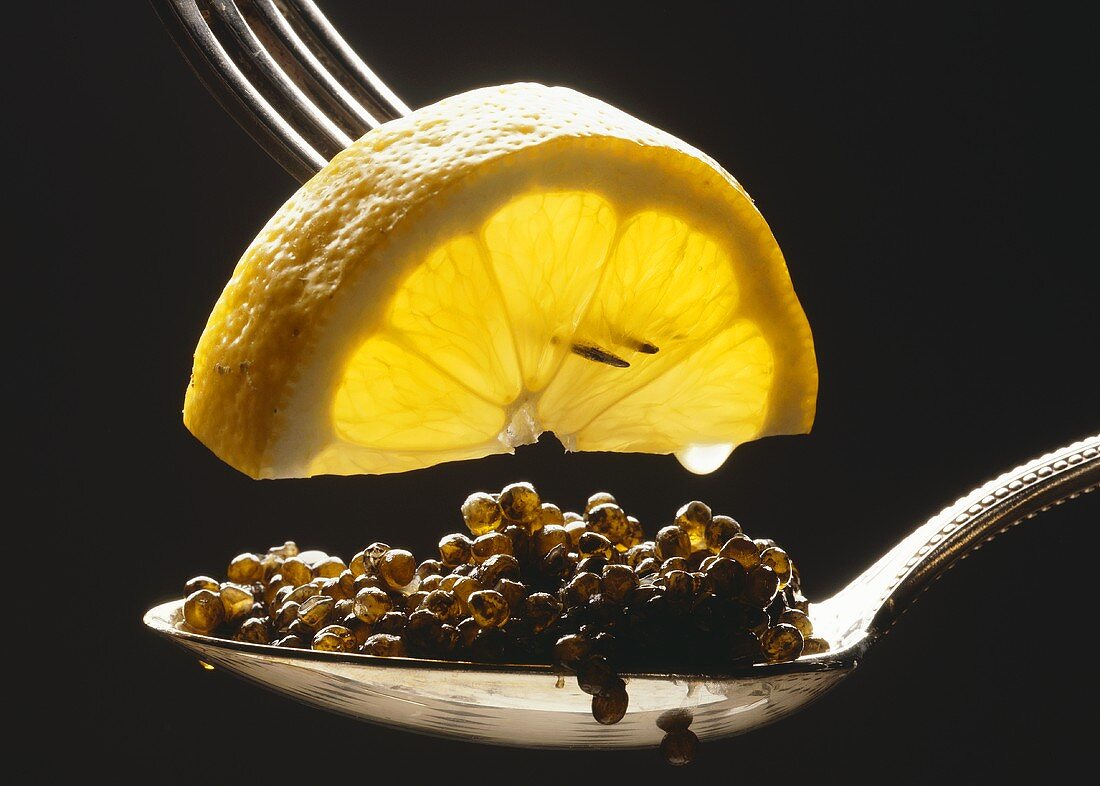 Ein Löffel Kaviar, darüber Zitronenschnitz auf Gabel