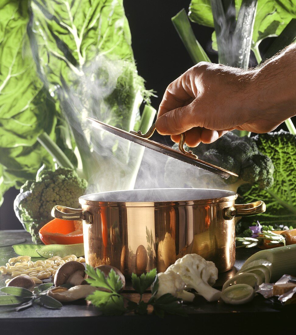 Hand lifting the lid of a steaming pan, with vegetables