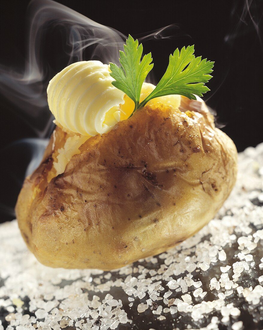 Dampfende Folienkartoffel mit Butter auf grobem Salz