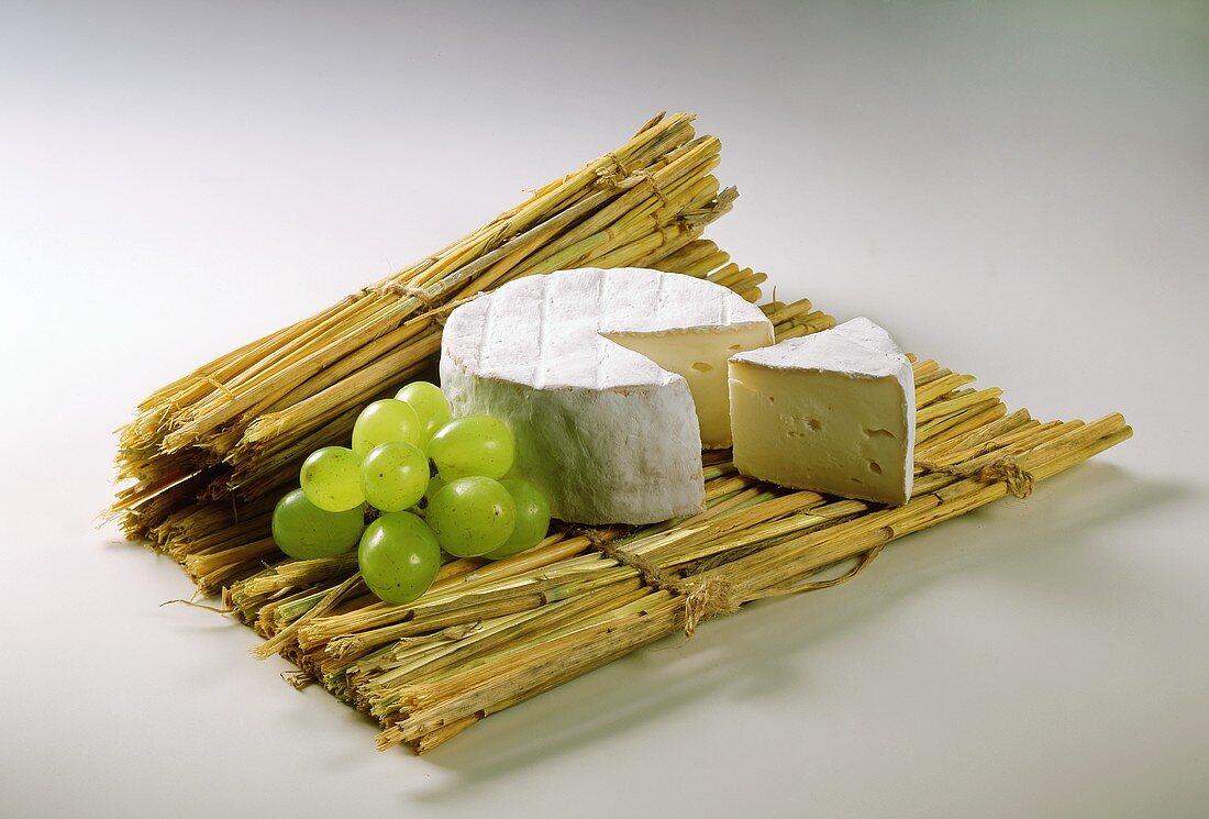 Camembert with piece cut out on straw mat; grapes