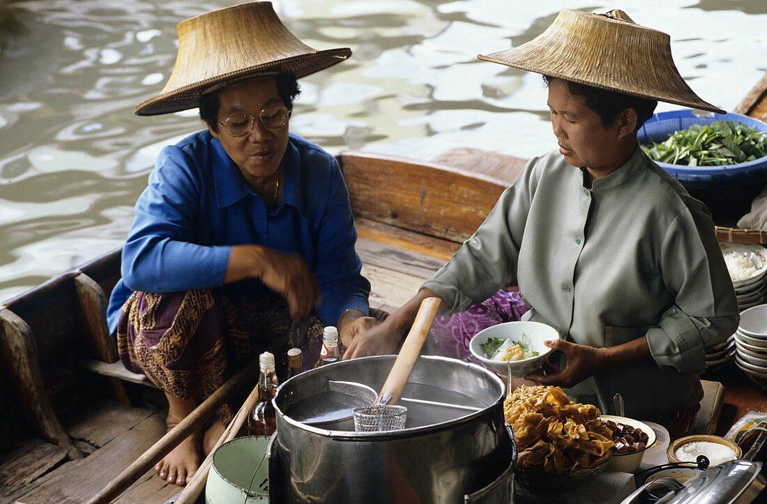 Thailänderinnen kochen Suppe auf einem Boot