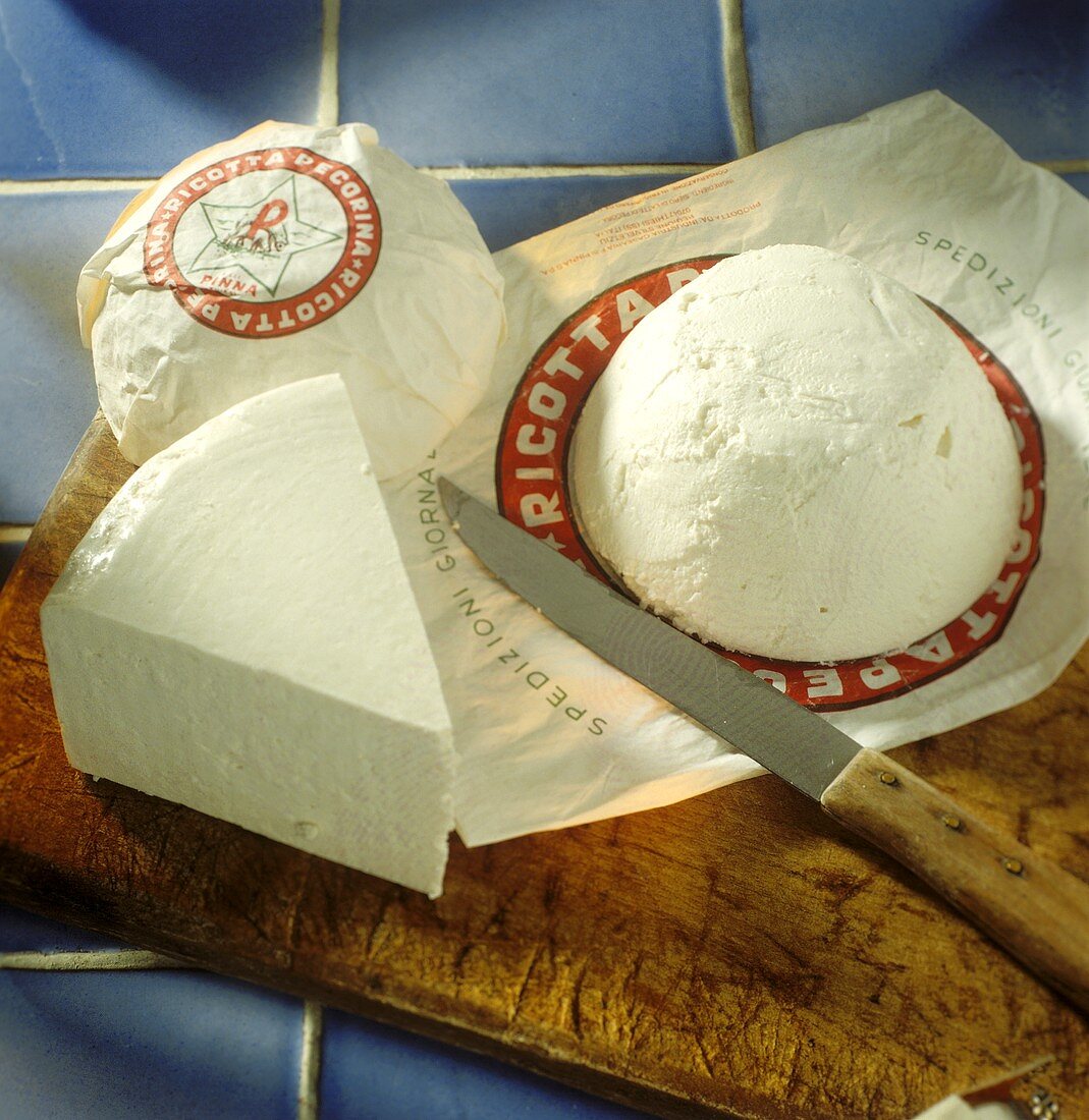 Ricotta, packed and unpacked, with knife on wooden board