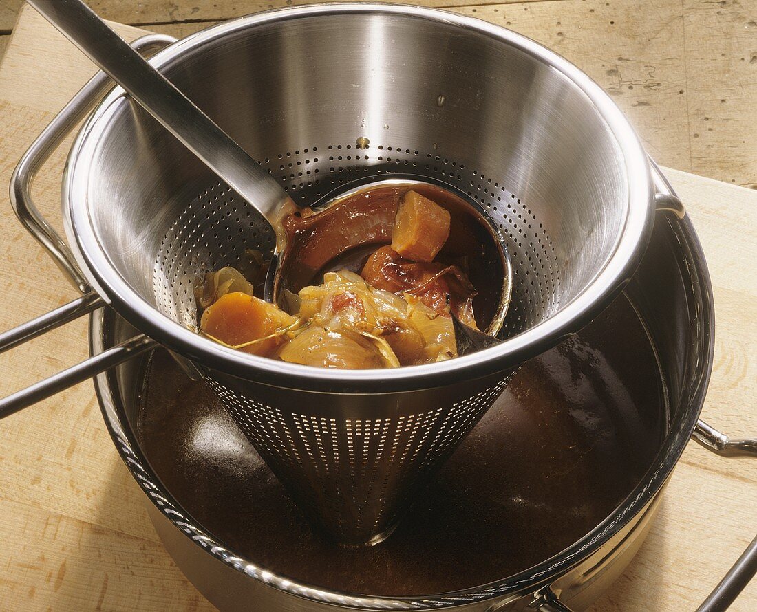 Boiled vegetables with ladle in a sieve (straining sauce)