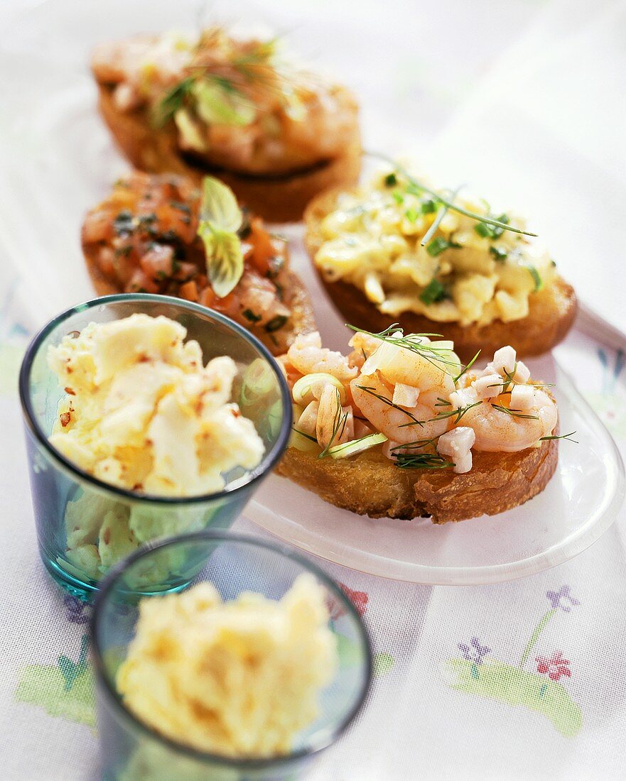 Vier verschiedene Crostini mit Rührei, Krabben und Tomaten