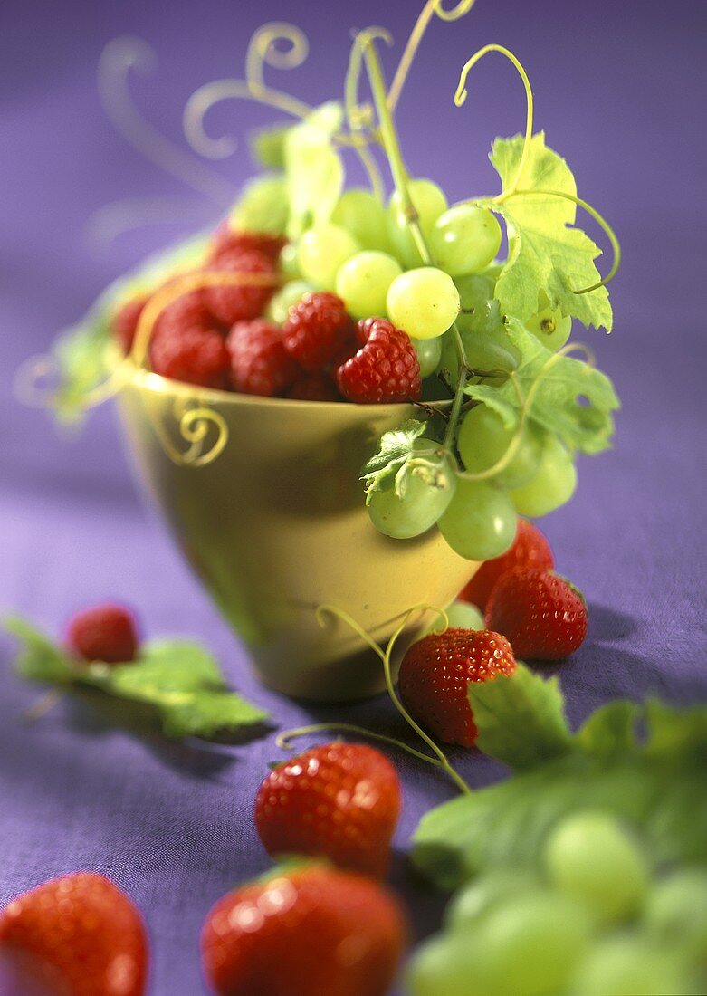 Green grapes, strawberries and raspberries in a yellow cup