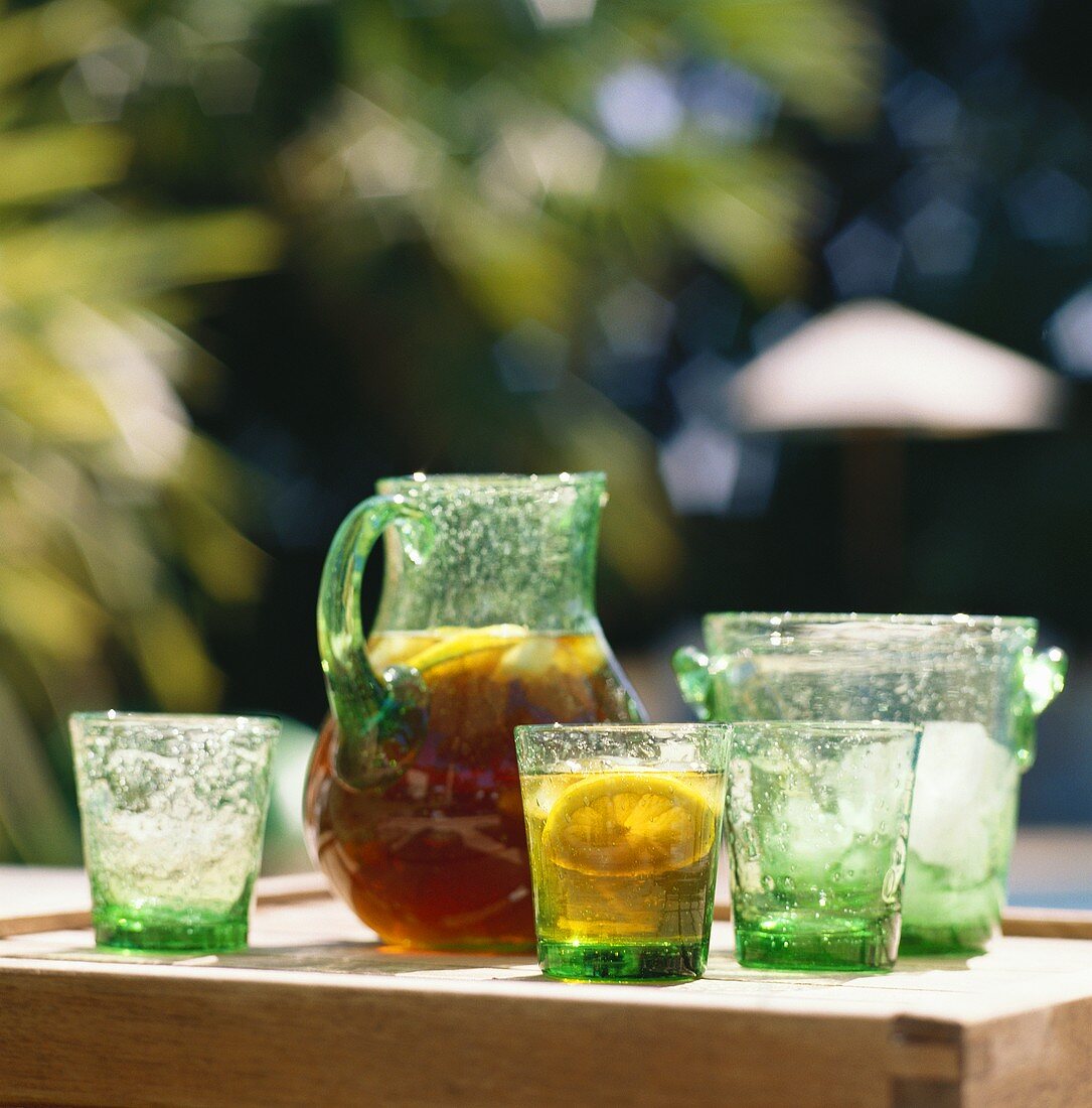 Eistee mit Zitrone im Glaskrug auf Tisch; Gläser; Eiskübel
