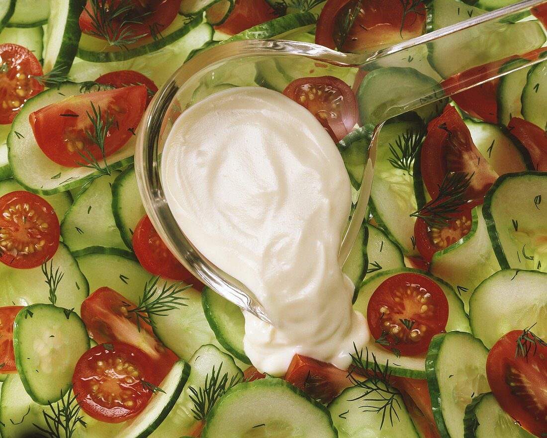 Salad dressing on ladle above tomato and cucumber salad