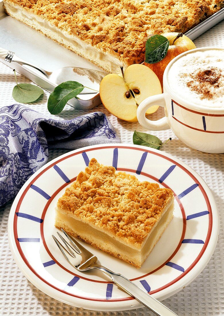 Apple cake with crumble on plate & baking sheet; cappuccino