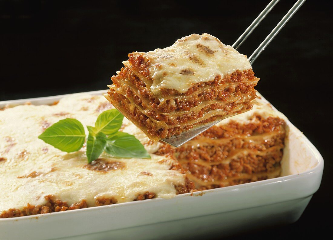 Lasagne with basil in baking dish, piece on server above it