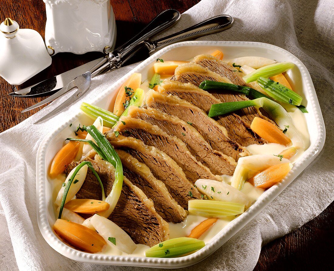 Sliced boiled beef fillet with vegetables on white platter