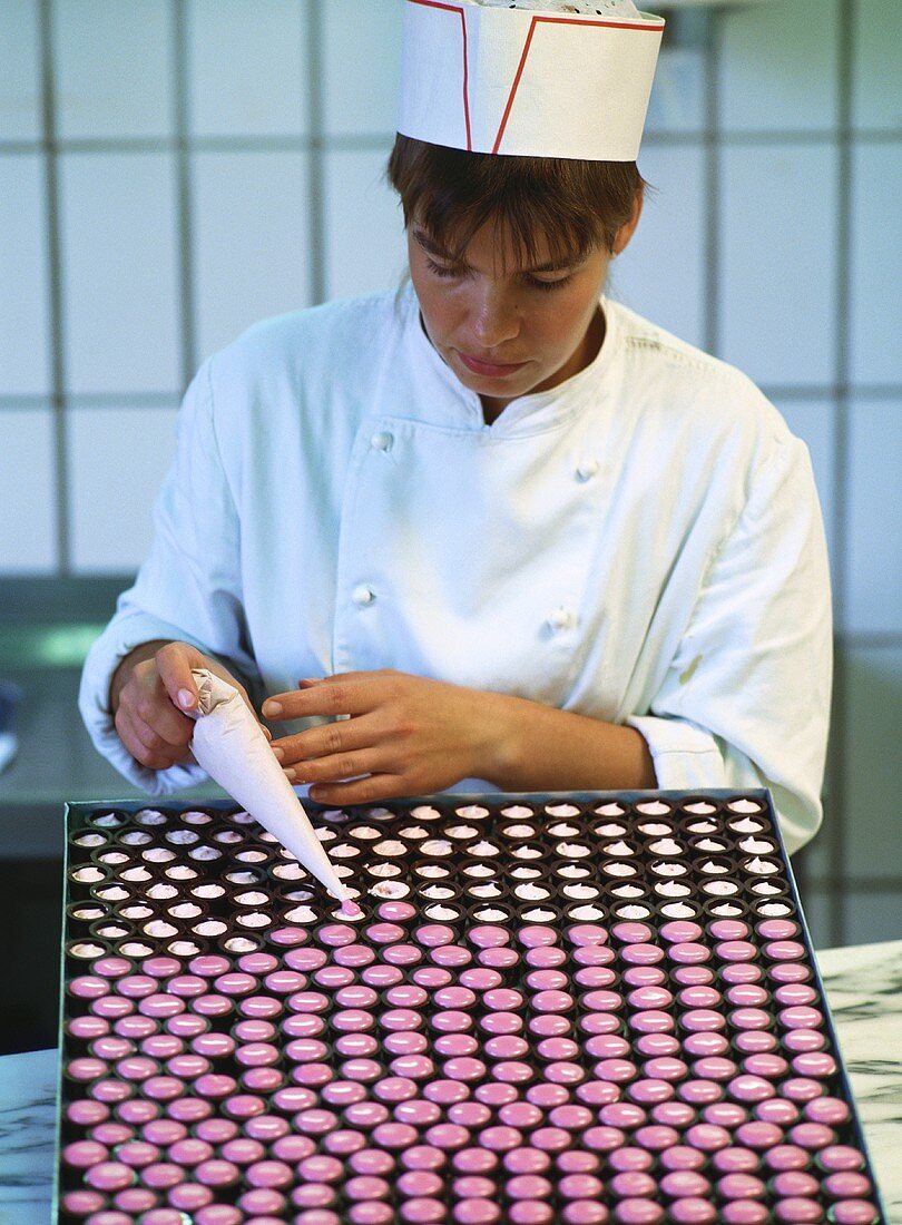 Female confectioner decorating chocolates with piping bag