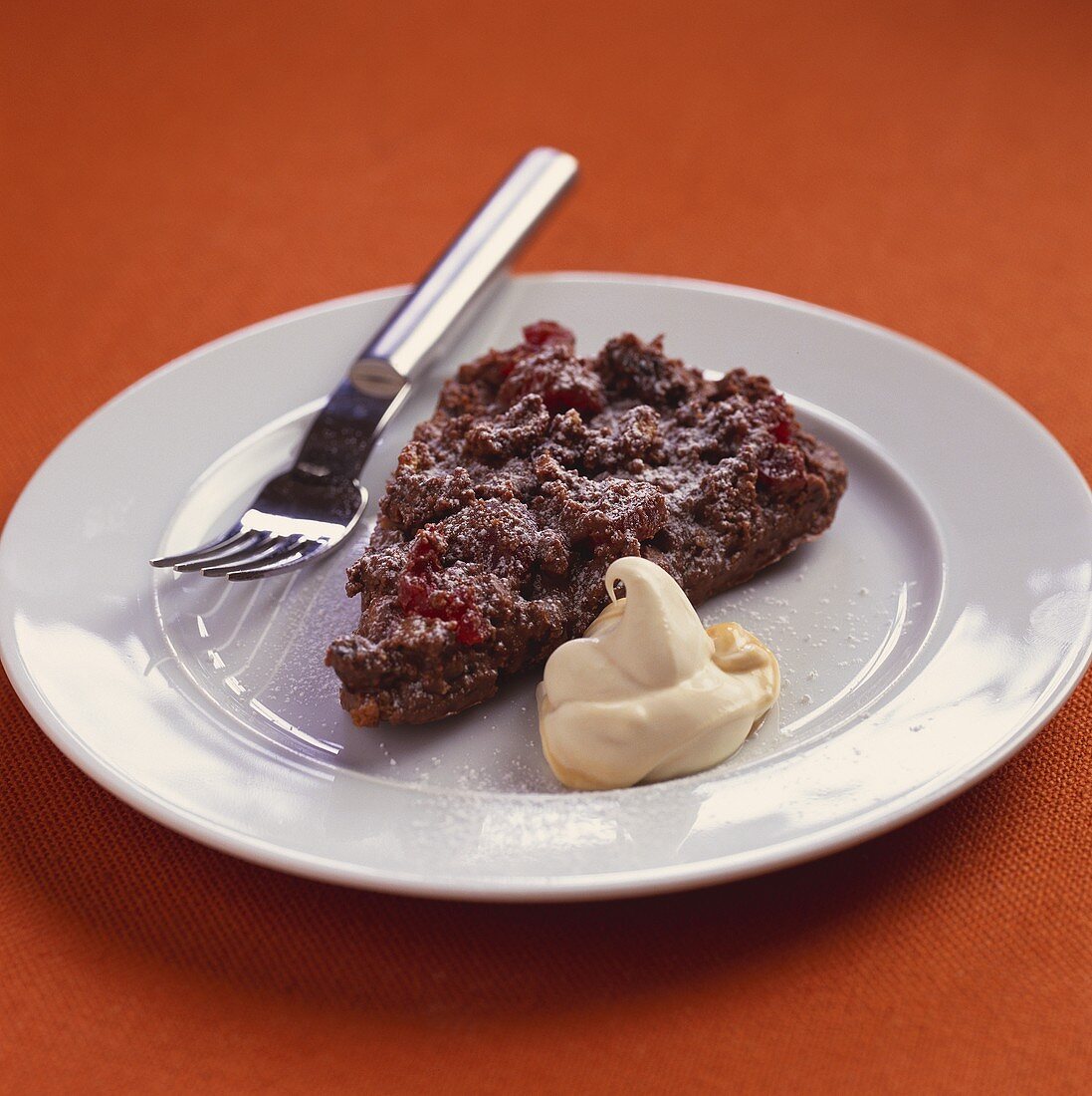 A piece of chocolate cherry cake with blob of cream on plate