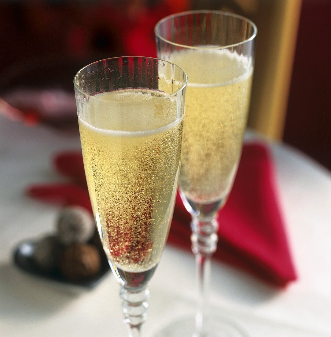 Two champagne glasses on a table in front of red napkin