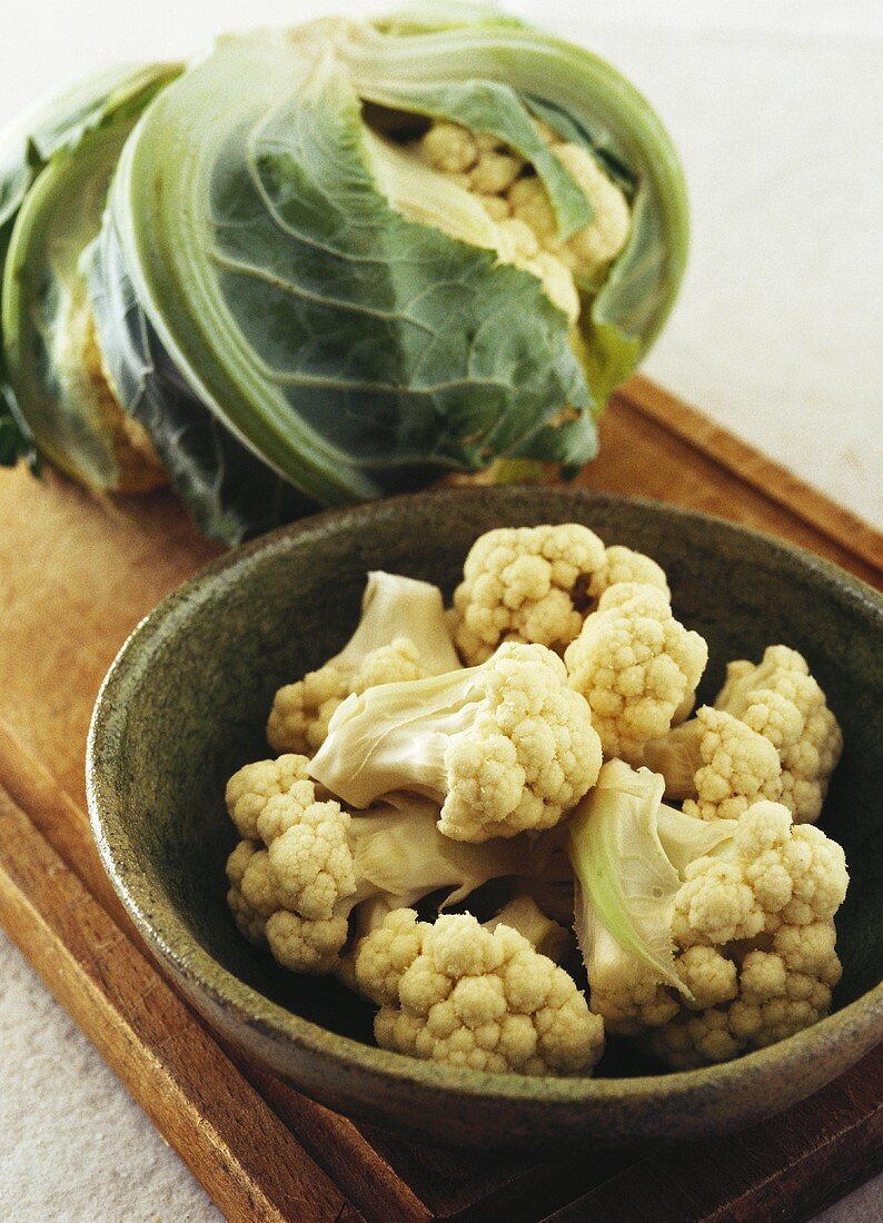 Cauliflower florets in brown bowl in front of whole cauliflower