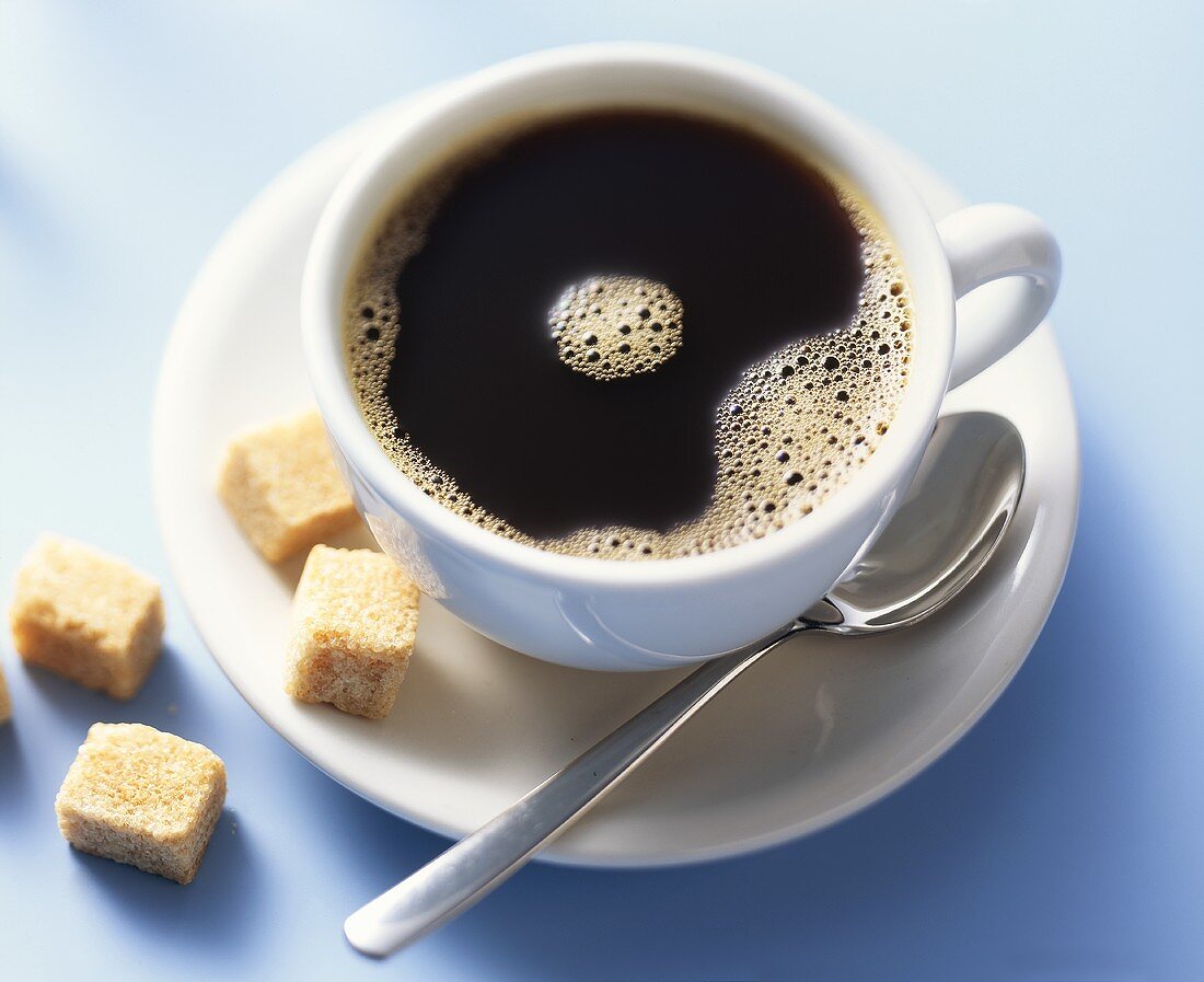 A cup of black coffee with raw cane sugar cubes