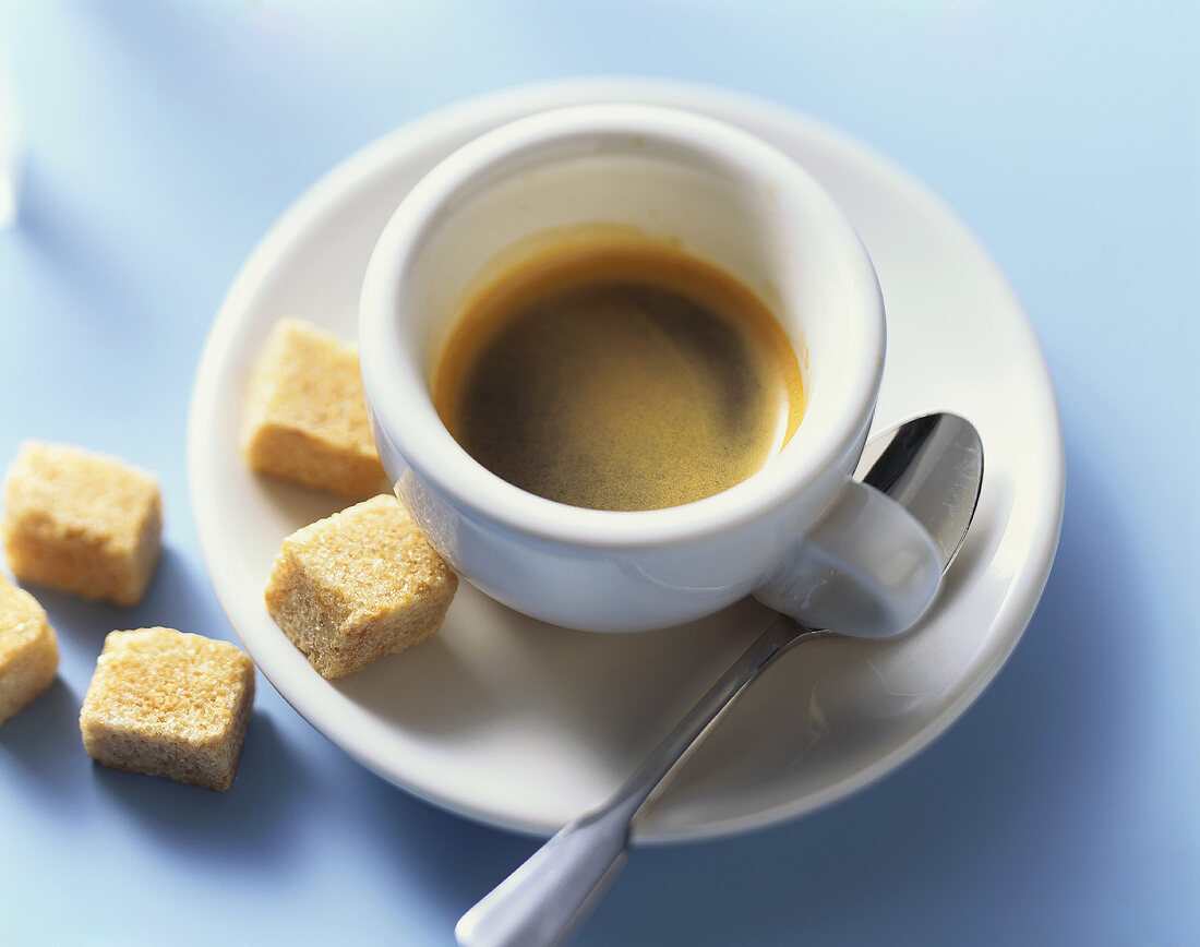 A cup of espresso with raw cane sugar cubes