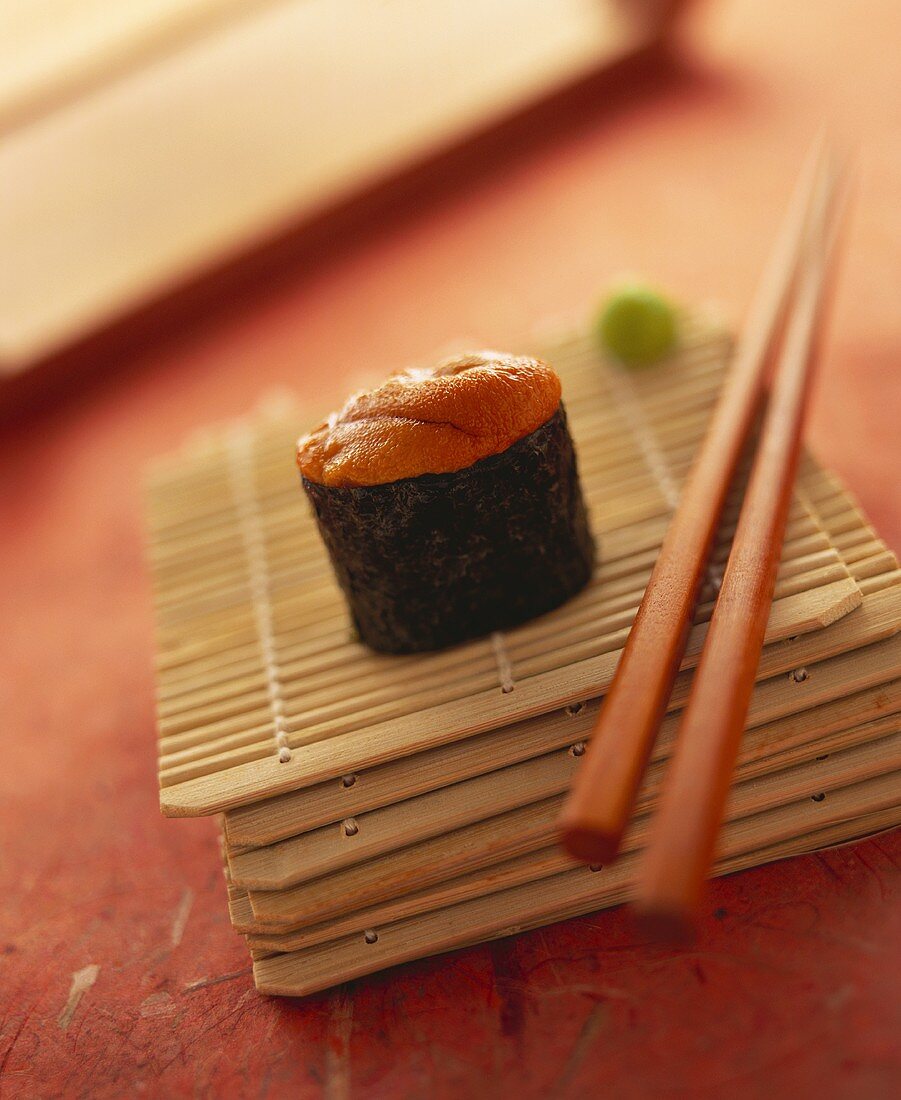 Ein Gunkan Maki mit Seeigel auf Bambusmatte mit Stäbchen