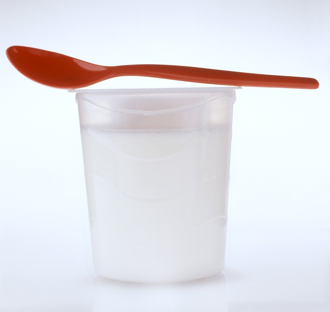 Ein Becher Joghurt mit rotem Plastiklöffel
