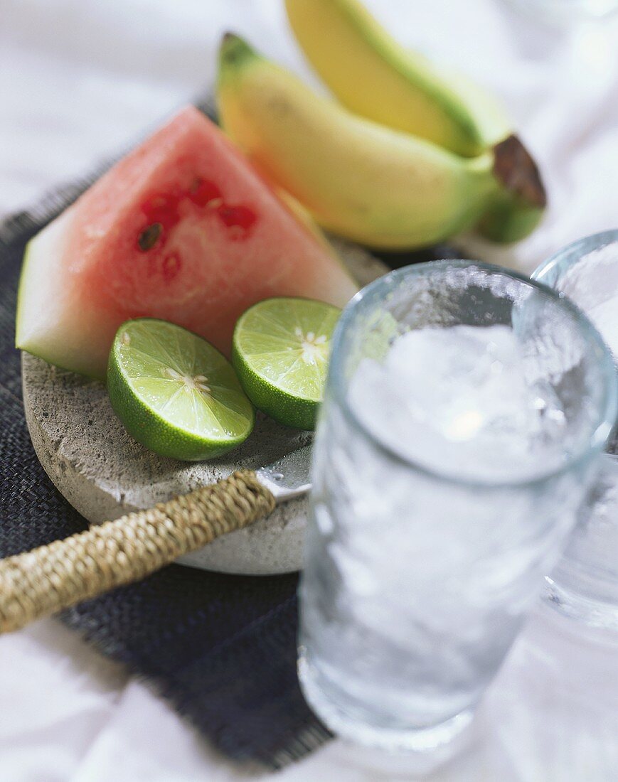 Limes, water melon, bananas and glass of ice cubes