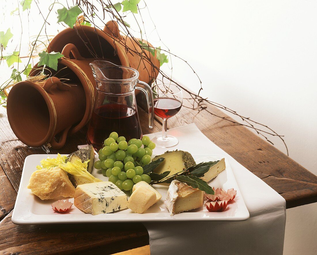 Cheese still life with grapes & red wine on wooden table; pots