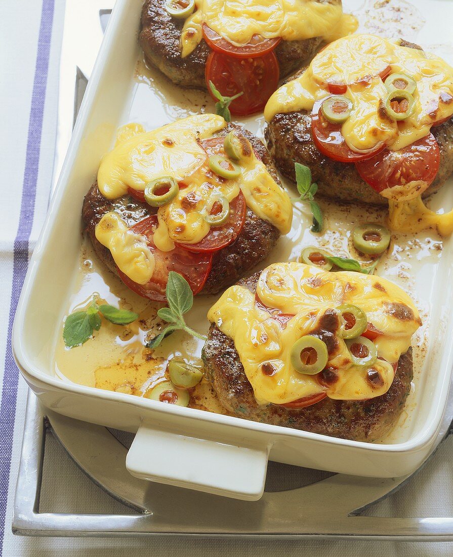 Vienna steaks gratinated with cheese, olives and tomatoes
