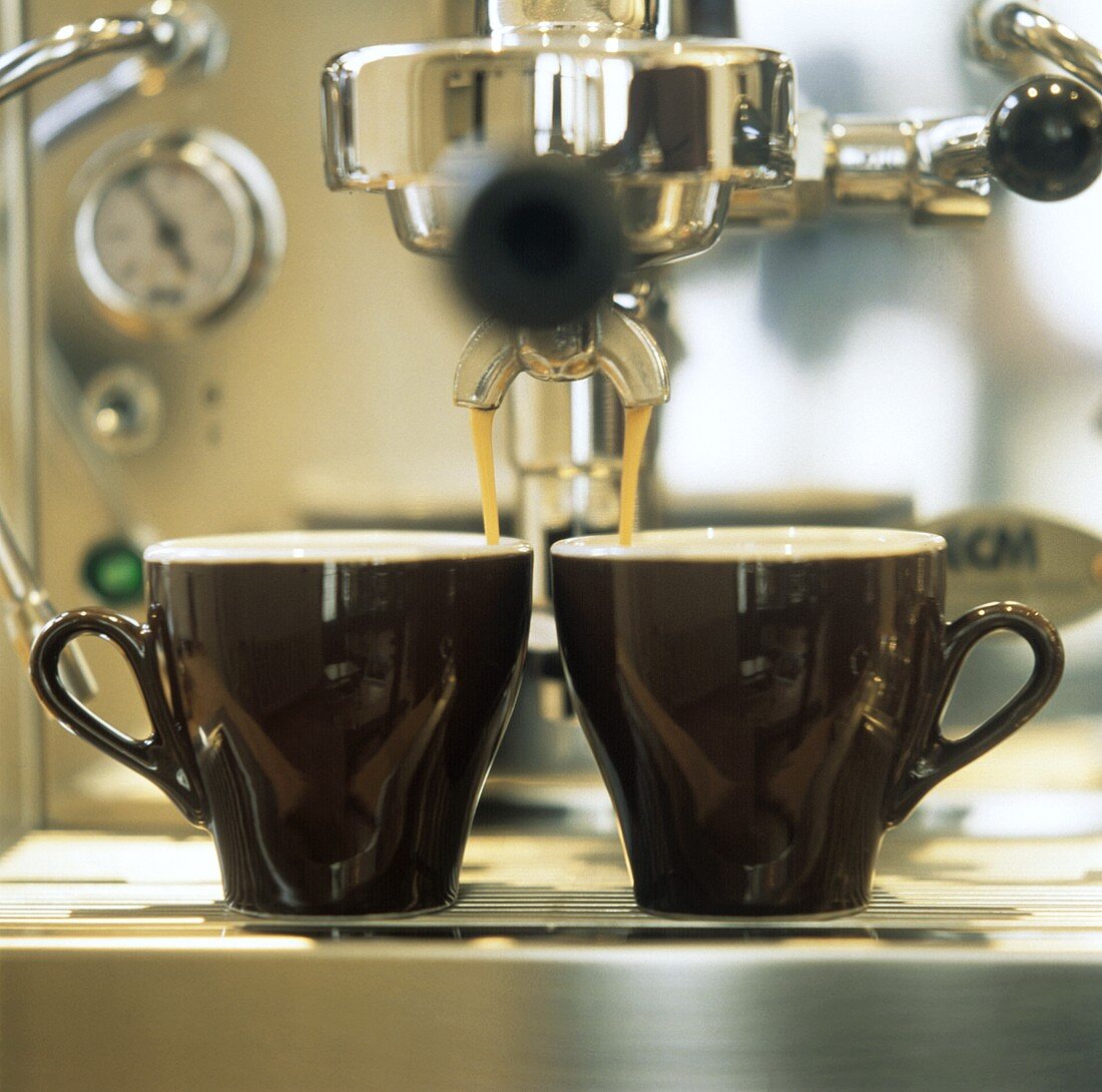 Espresso fliesst aus Espressomaschine in zwei Tassen