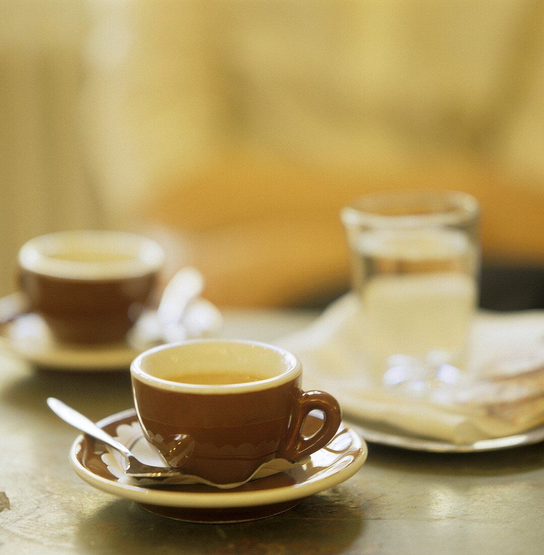 Zwei Espressotassen und ein Glas Wasser auf einem Tisch