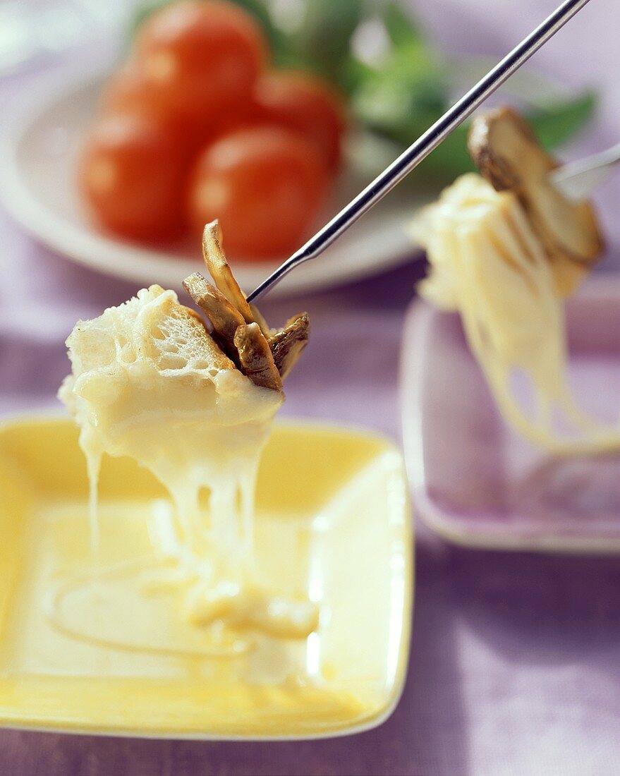Cheese fondue with mushrooms on fondue forks, vegetable plate