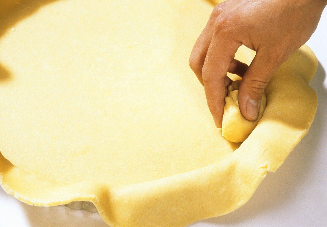 Pressing pastry on to inner edge of tart tin