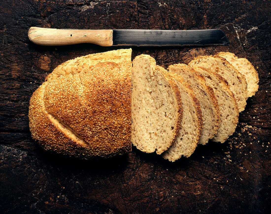 Sesame bread, partly sliced, on a wooden background
