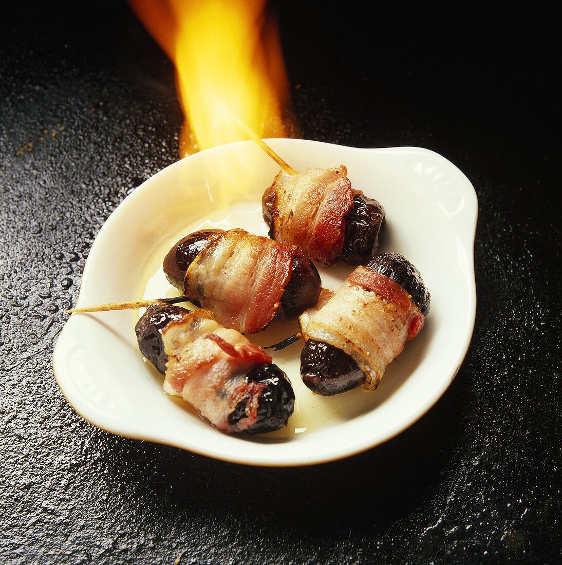 Flambéing bacon-wrapped plums on white plate