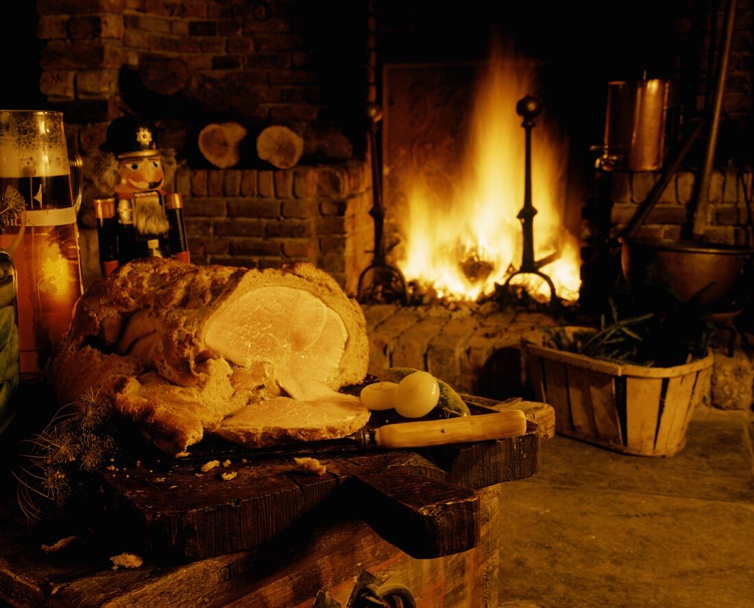 Schweinebraten im Brotteig auf Holzbrett vor Kamin