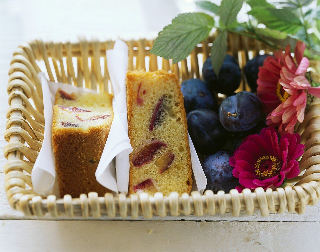 Plum cake, fresh plums and flowers in bread basket
