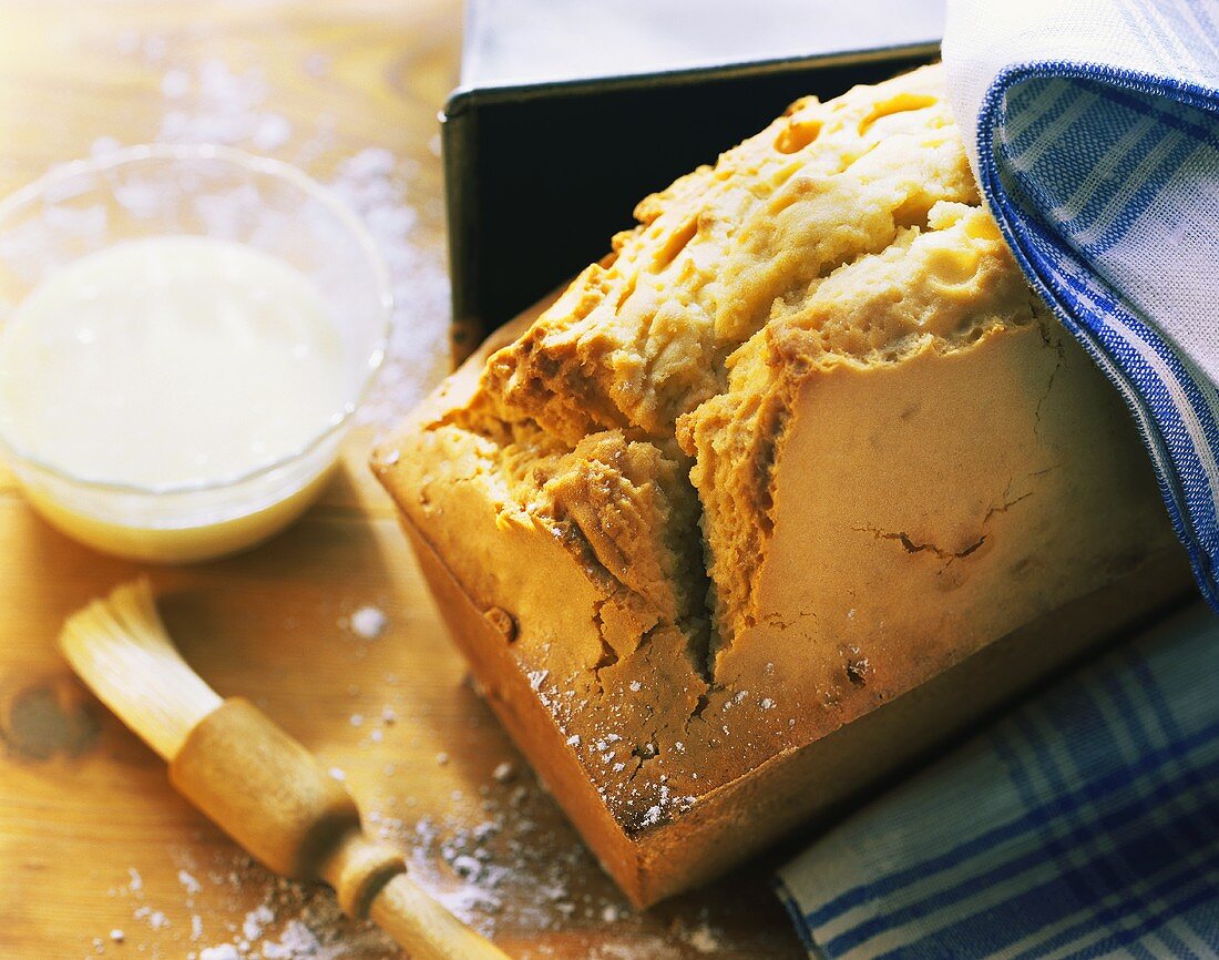 Sandkuchen neben Kastenform; Zuckerglasur und Backpinsel