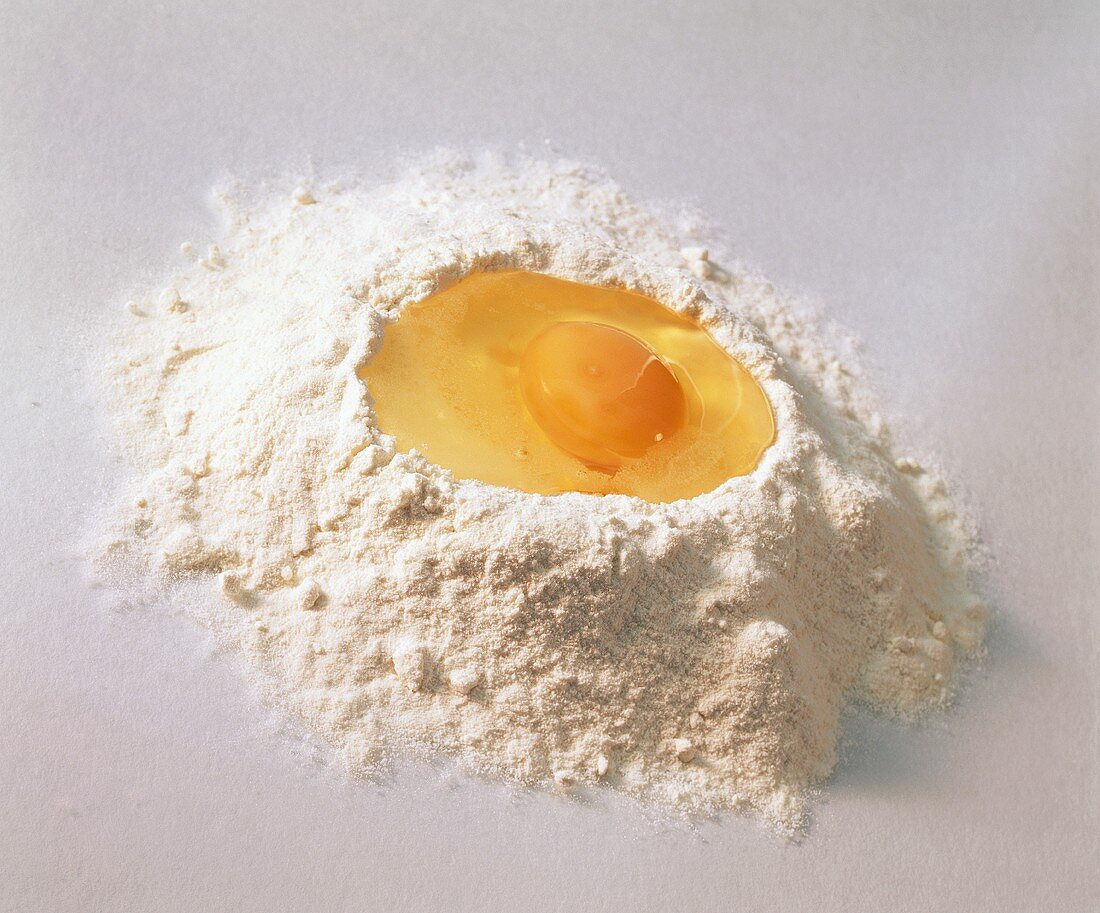 Aufgeschlagenes Ei in einem Häufchen Mehl