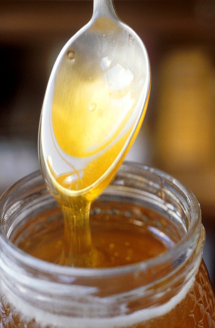 Honig fliesst vom Löffel ins Glas