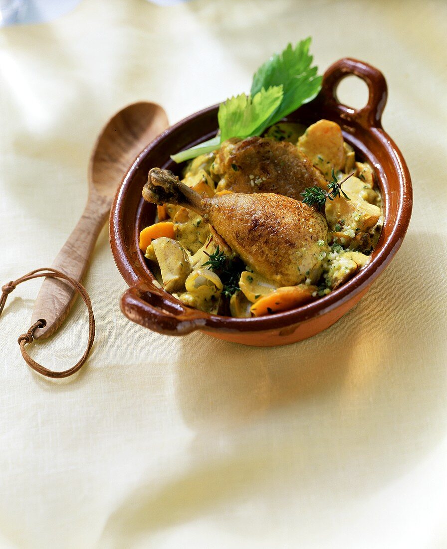 Chicken leg with vegetables in ceramic pot beside wooden spoon