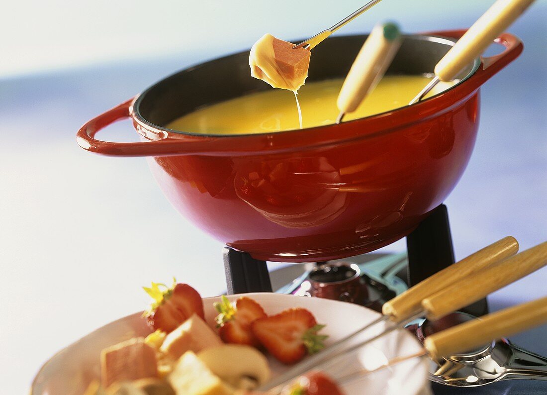 Cheese fondue with ham and strawberries in fondue pot