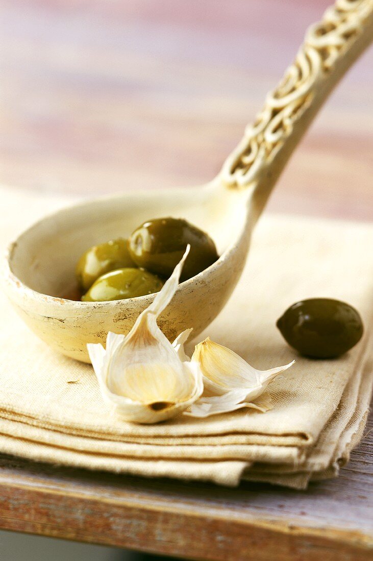 Grüne Oliven auf Kelle; Knoblauchzehen auf Leinenservietten