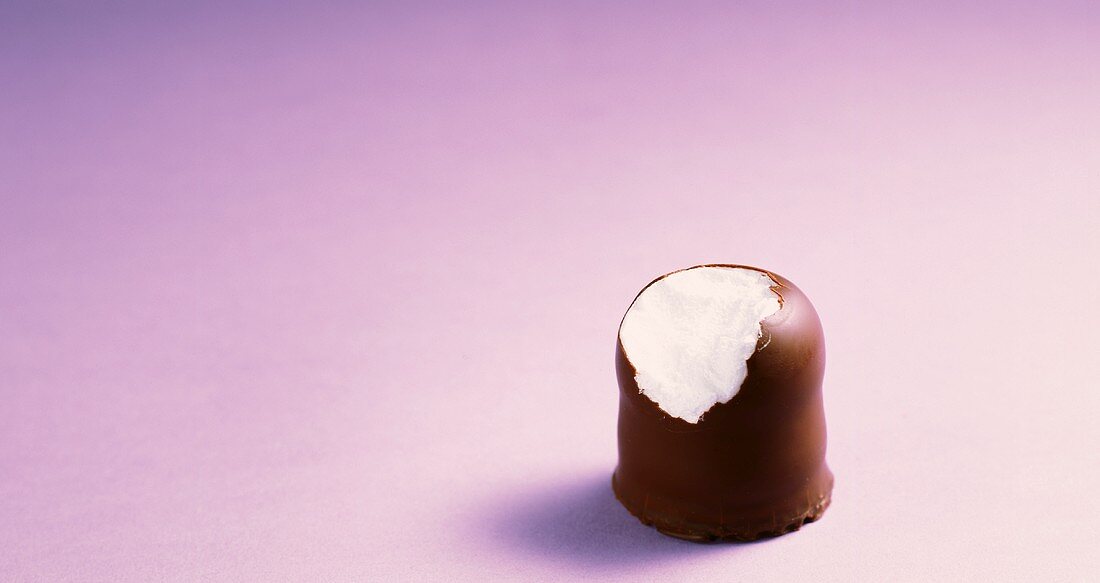 Chocolate marshmallow on mauve background (a bite taken)