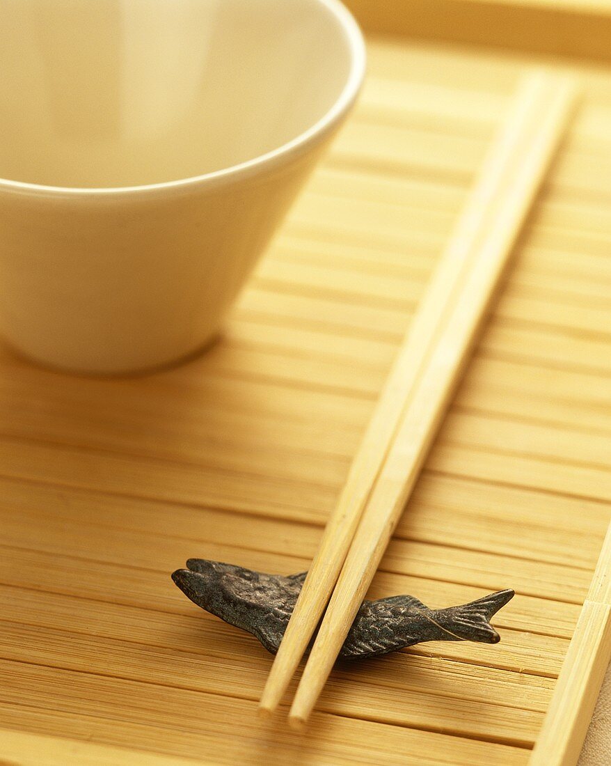 Chopsticks, fish decoration & white bowl on wooden background