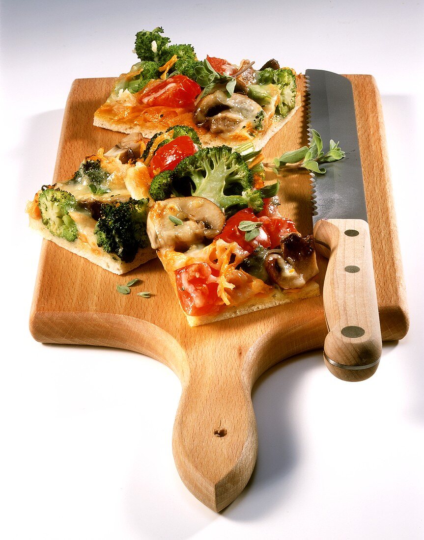 Colourful vegetable pizza in pieces on chopping board
