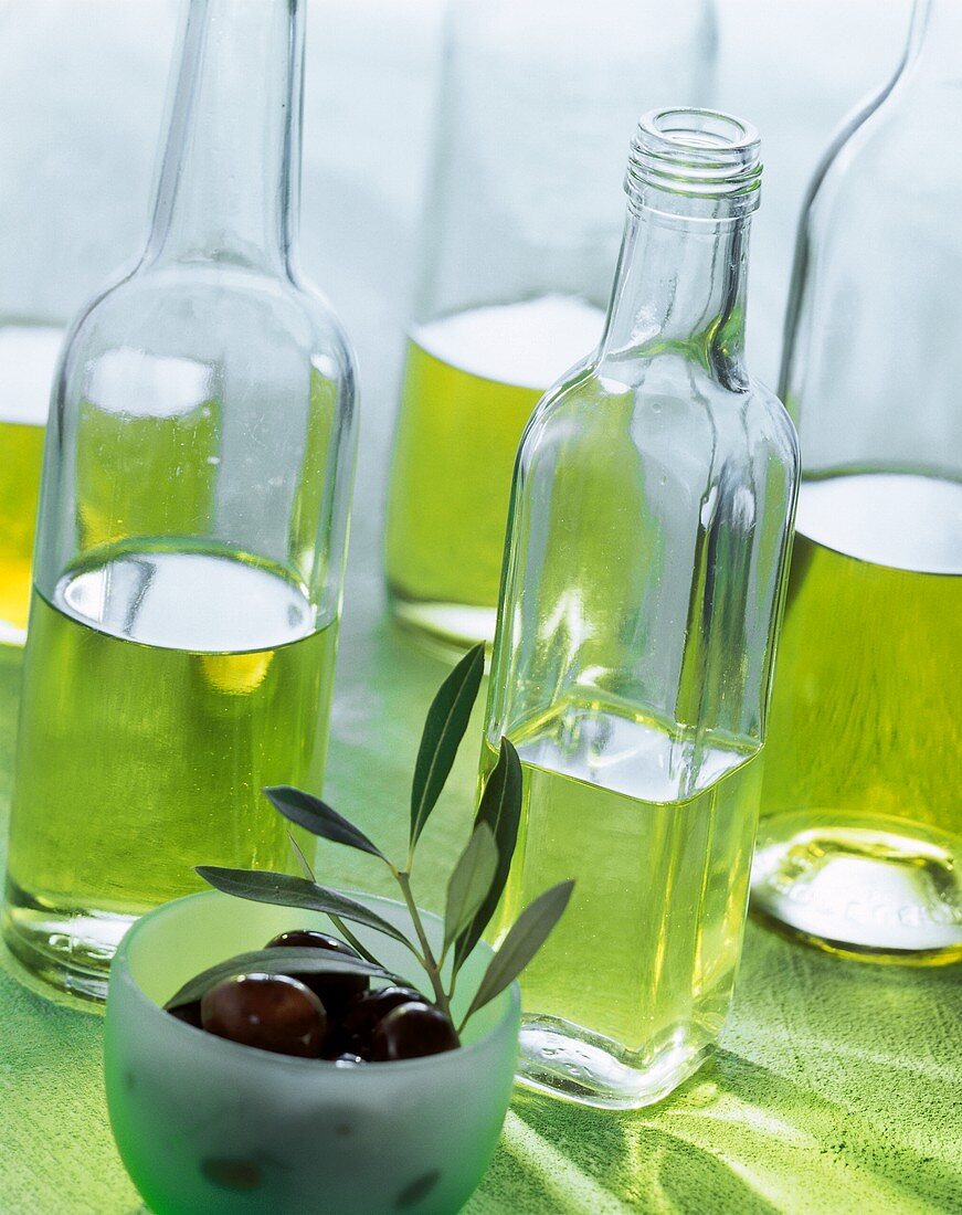 Various types of olive oil in bottles; black olives